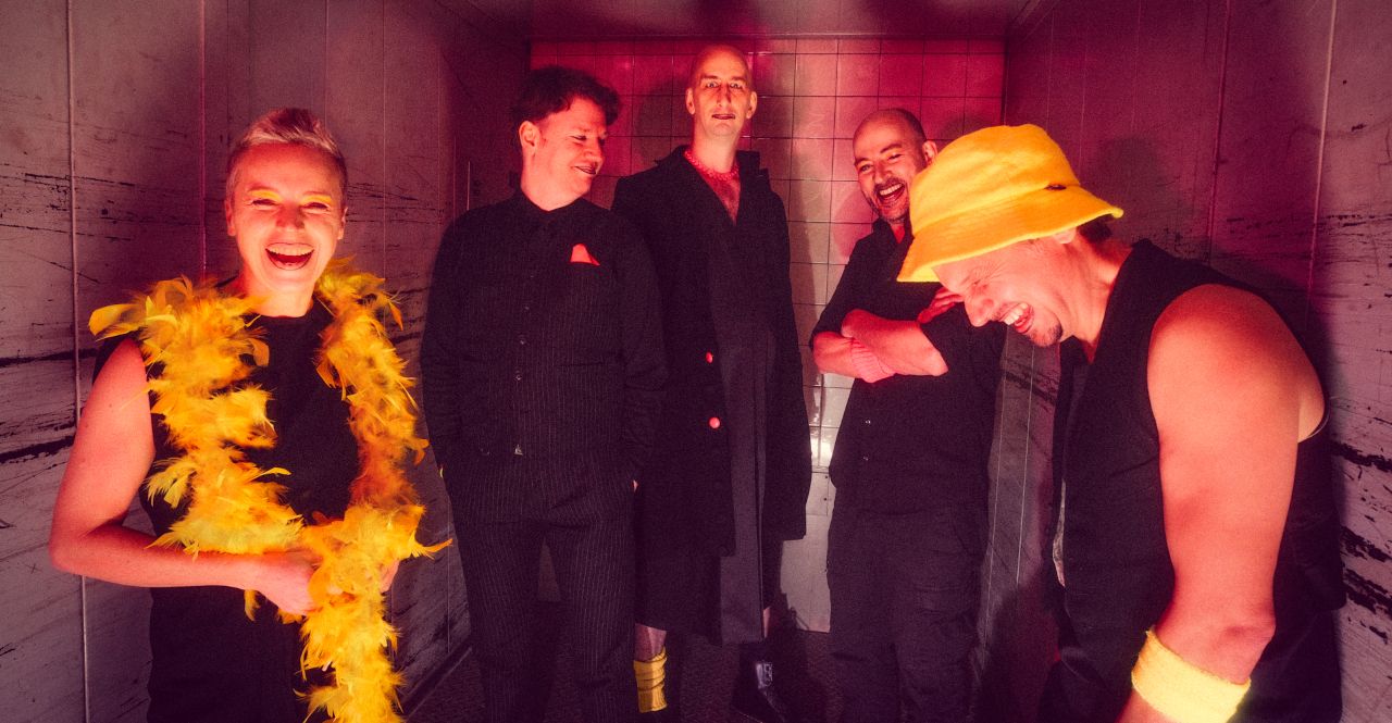 Das VPT-Ensemble in schwarzen Klamotten mit gelben und pinken Highlights steht lachend im Lastenaufzug. Foto: Norman Tebel